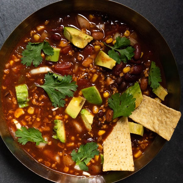 Bowl of chili with beans, cilantro, and tortilla chips.